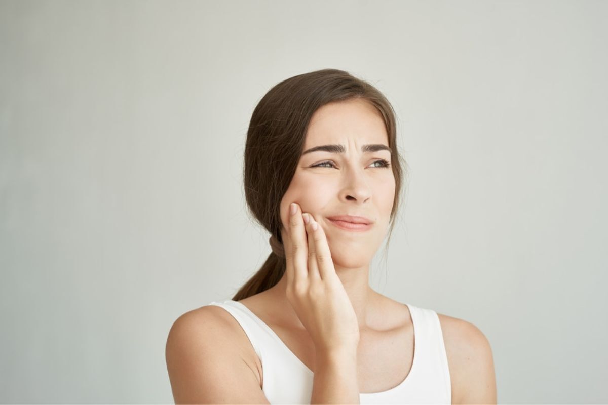 Woman with jaw pain touching her cheek, illustrating TMJ disorder symptoms.