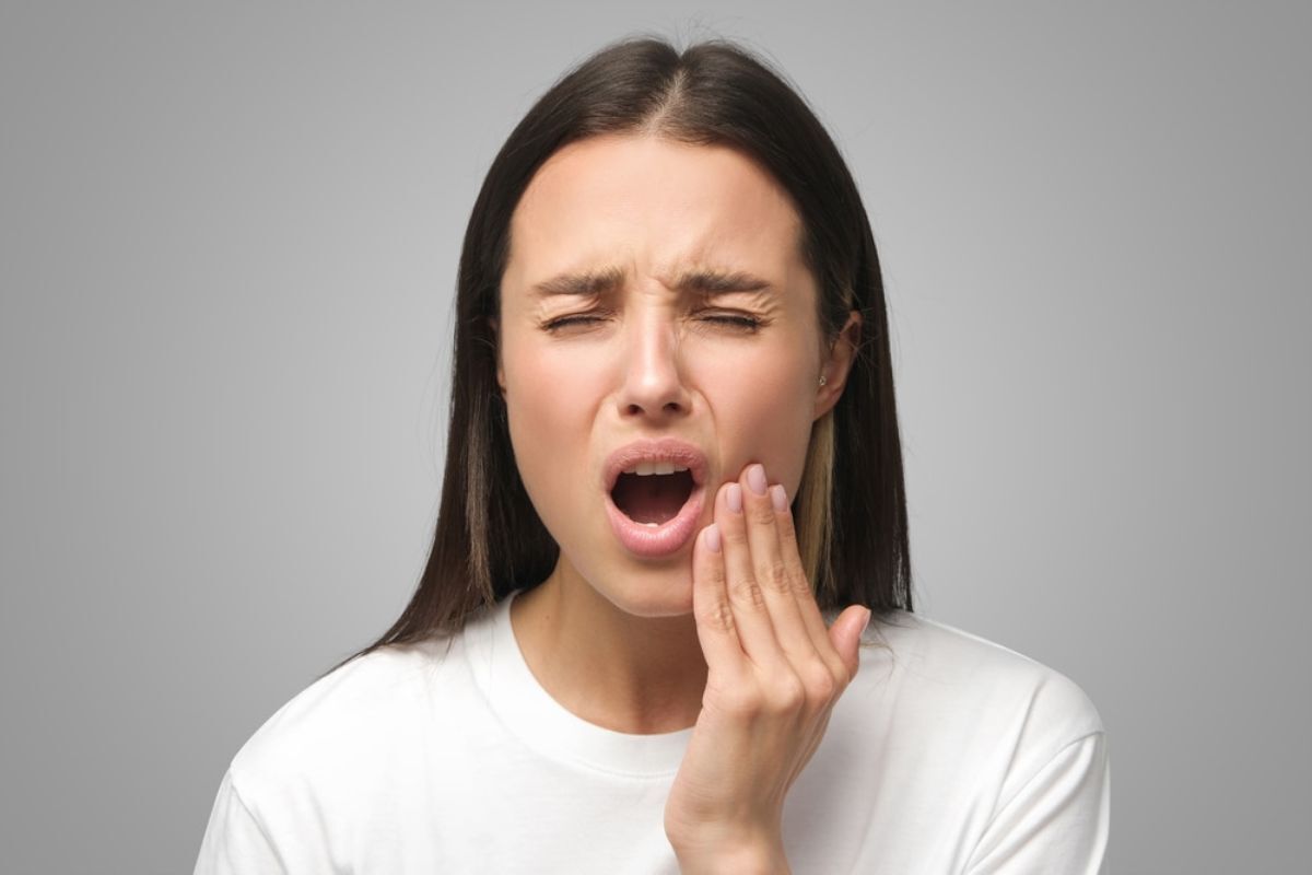 TMJ Treatment Duxbury Woman experiencing jaw pain touching her cheek during TMJ discomfort.