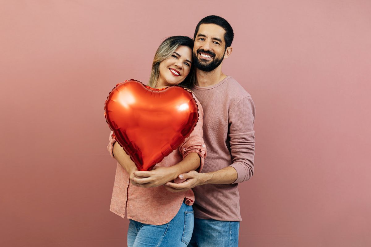 Smiling couple holding red heart balloon for Valentine's Day dental promotion in Duxbury.