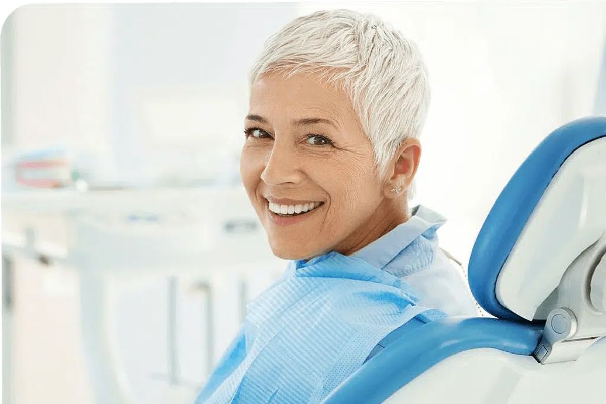 Smiling mature woman in dental chair during implant or bridge consultation at Duxbury dental practice.