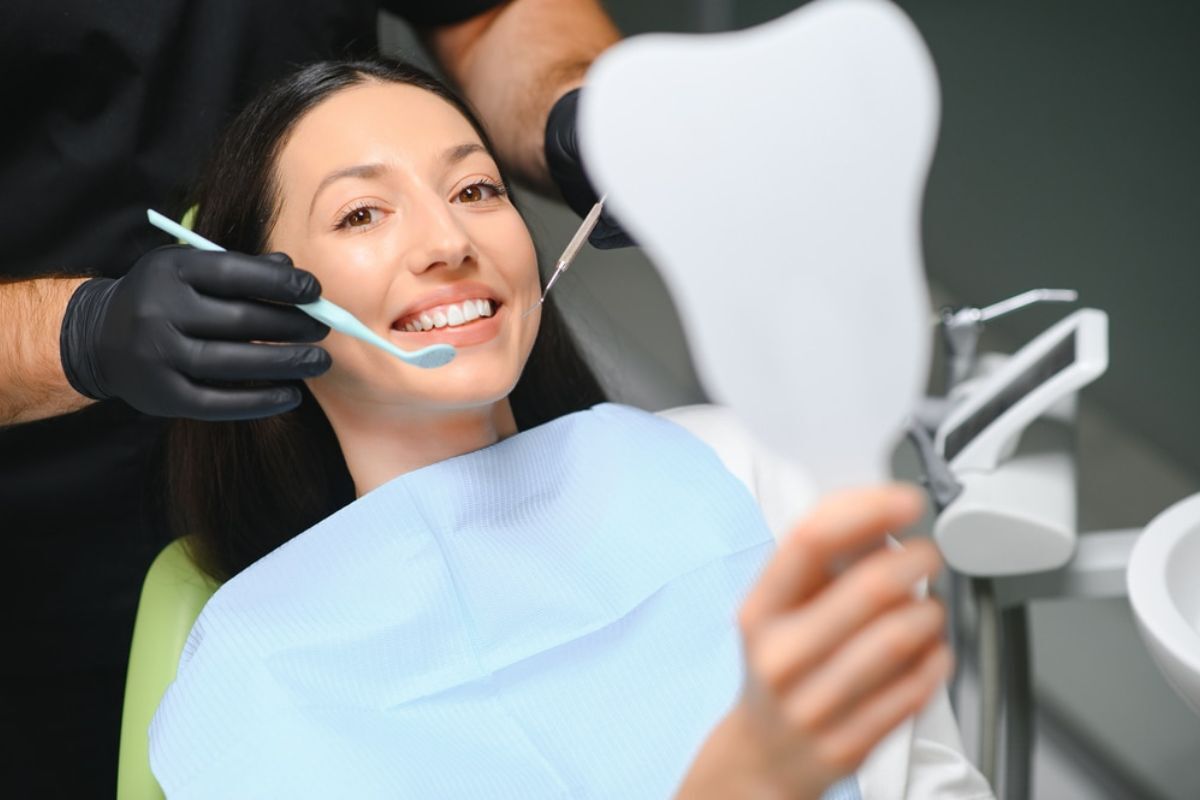 Patient admiring her bright smile in mirror after cosmetic dental treatment in Duxbury.