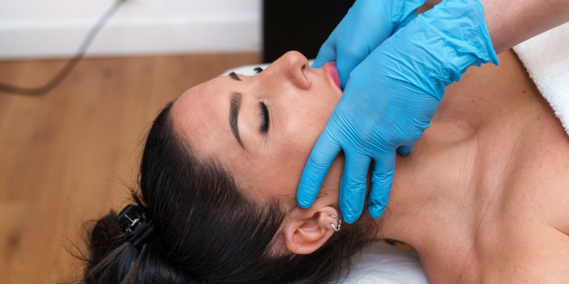 Dentist examining patient's jaw and face to diagnose TMJ disorder treatment needs.