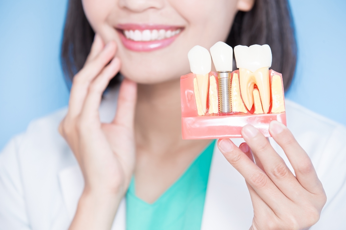 Woman displaying dental implant model showing tooth replacement with crown and titanium screw.