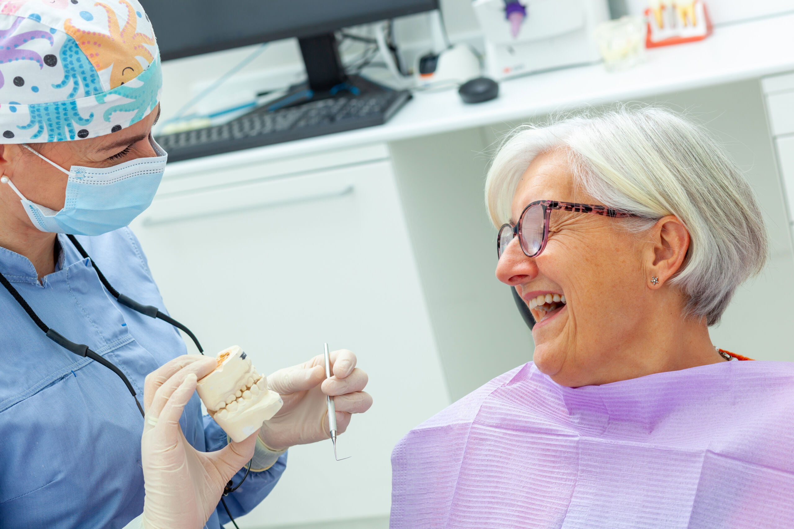 Dentist showing dental implant model to smiling senior patient in Duxbury.
