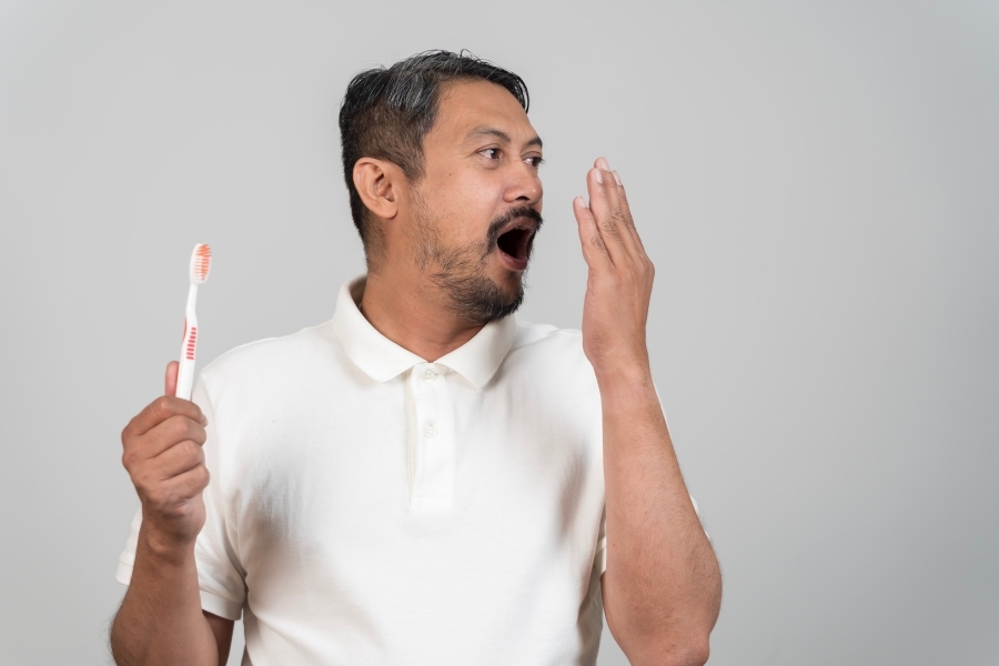 Man with shocked expression holding toothbrush, checking breath awareness.