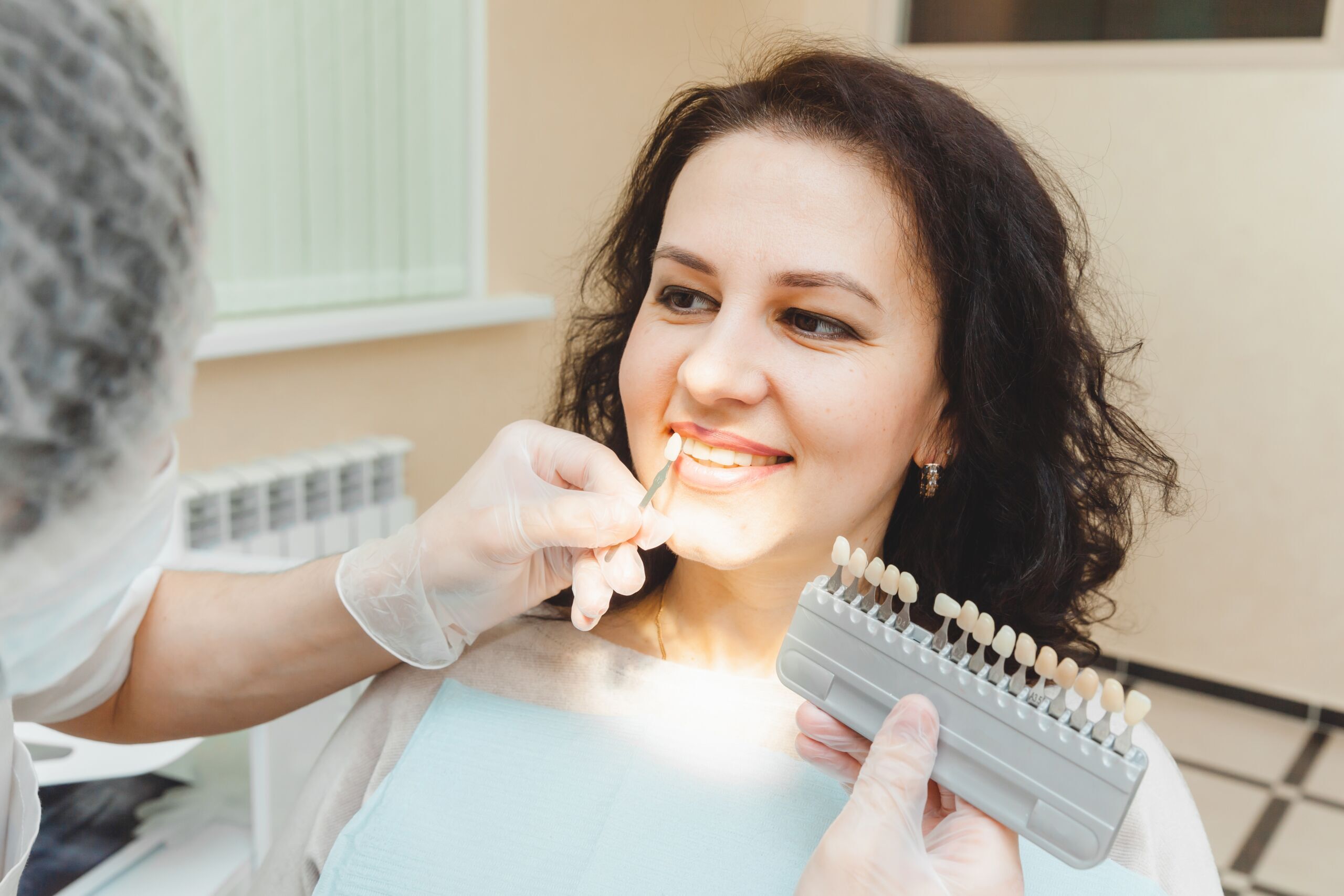 Dentist comparing tooth shade samples with smiling patient during cosmetic consultation.