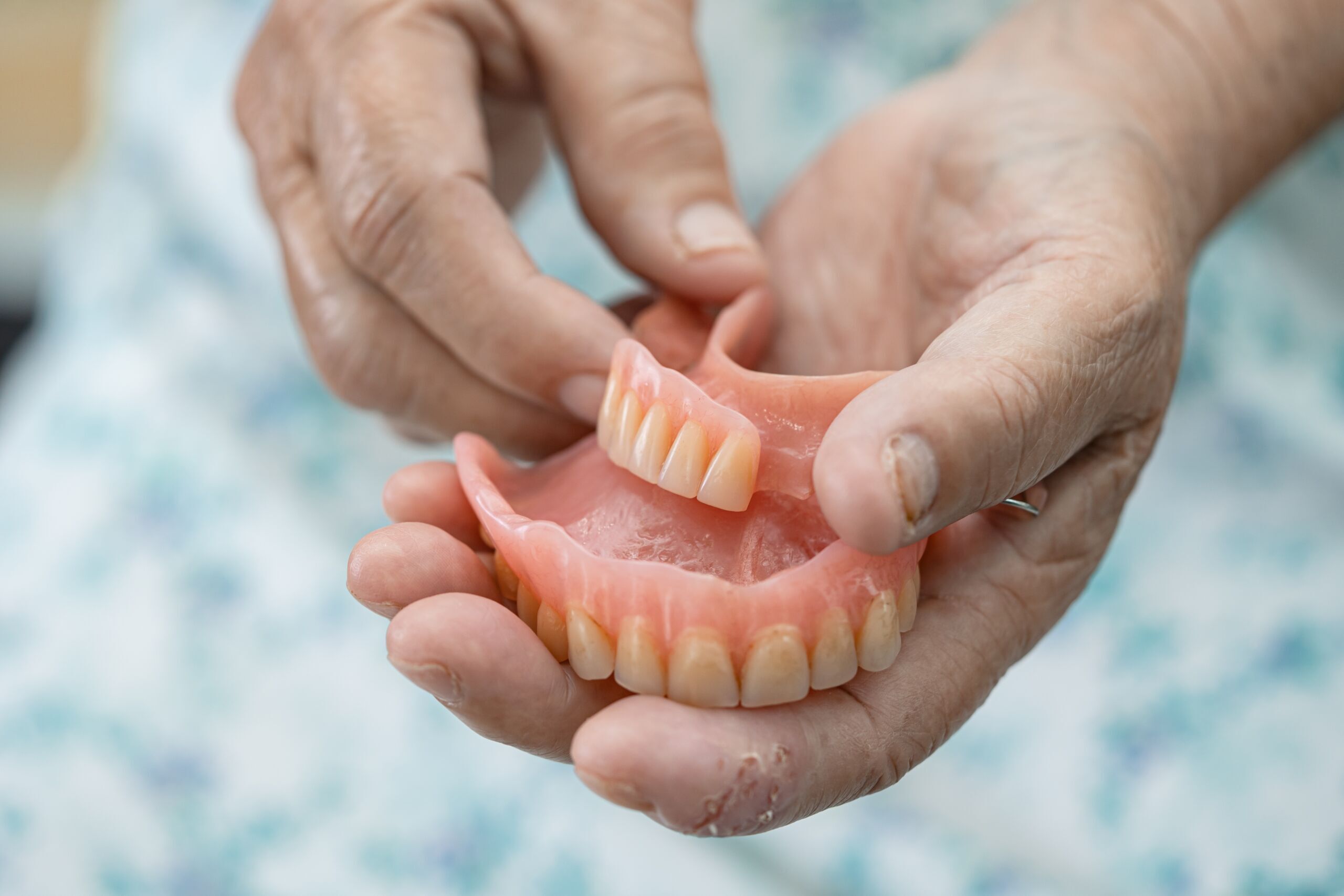 Asian senior or elderly old woman patient holding to use denture Hands holding a full denture showing replacement teeth in a natural shade for smile restoration.