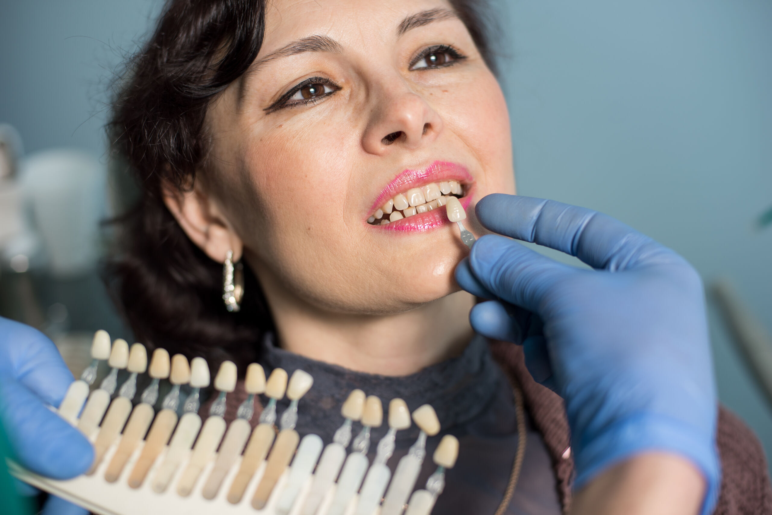 woman in dental clinic office. Dentist checking and selecting colour of the teeth. Dentistry Dentist showing patient tooth shade guide for dental implant or crown color matching.