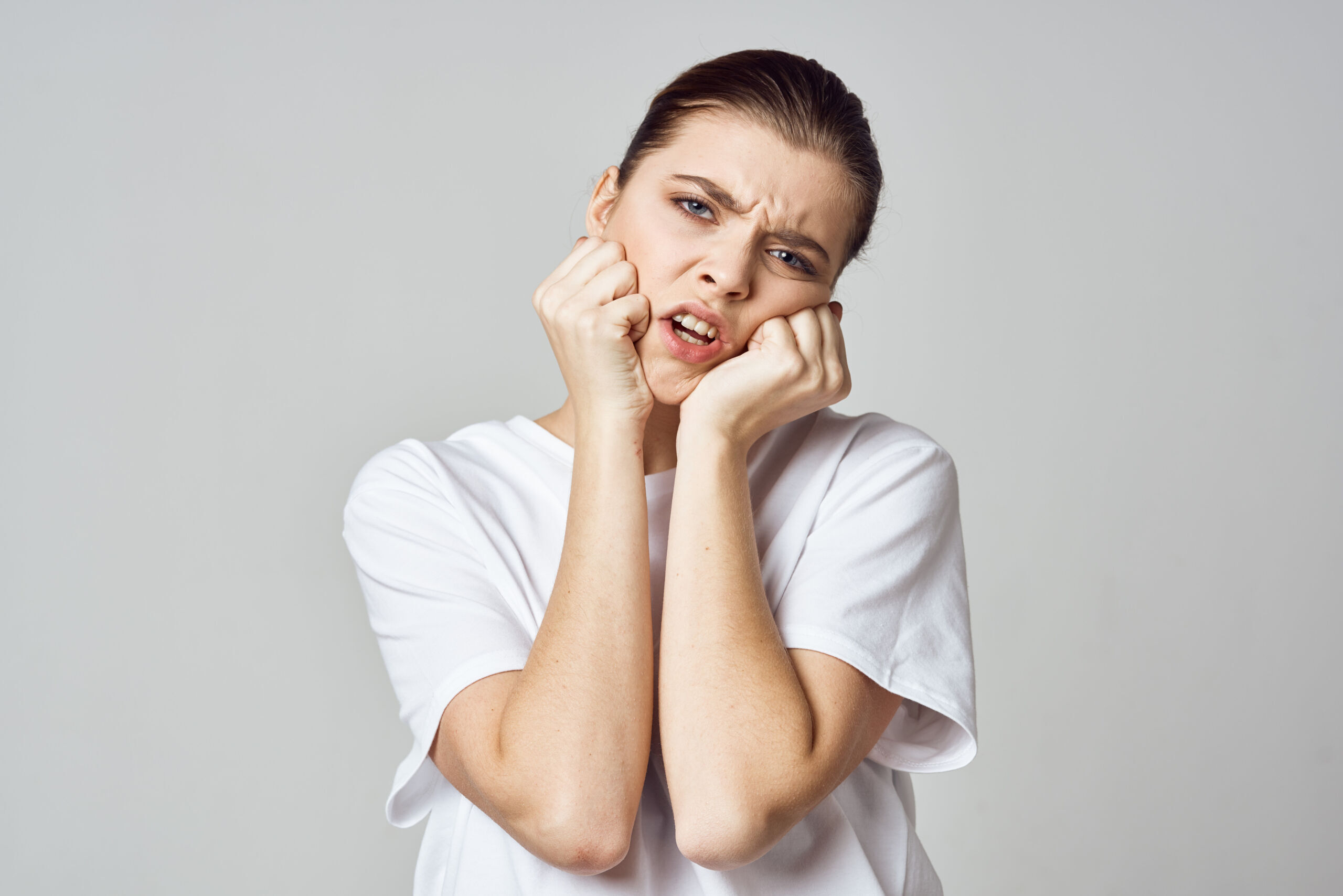 Woman with TMJ pain holding her jaw with both hands in discomfort.