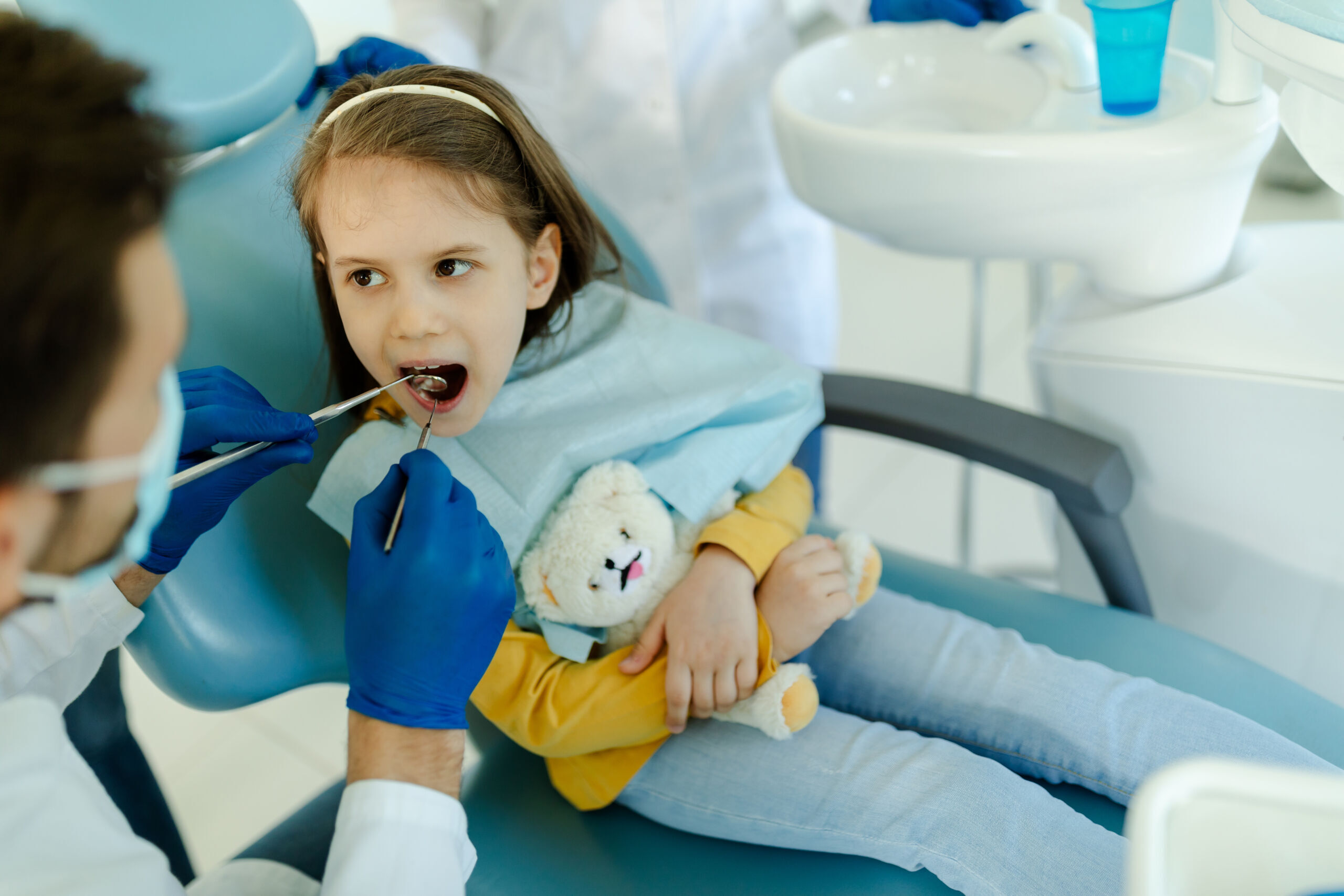 How to Make Kids Less Afraid of the Dentist: A Parent’s Practical Guide Young girl holding a stuffed animal during a dental examination in the treatment chair.