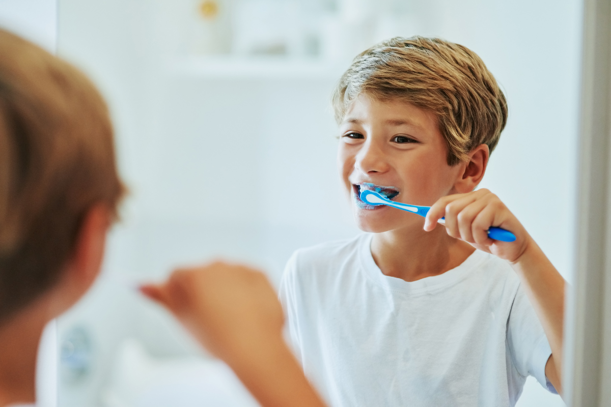 How Sugar Destroys Your Teeth — And How to Fight Back Young boy brushing his teeth with a blue toothbrush in a bathroom mirror.
