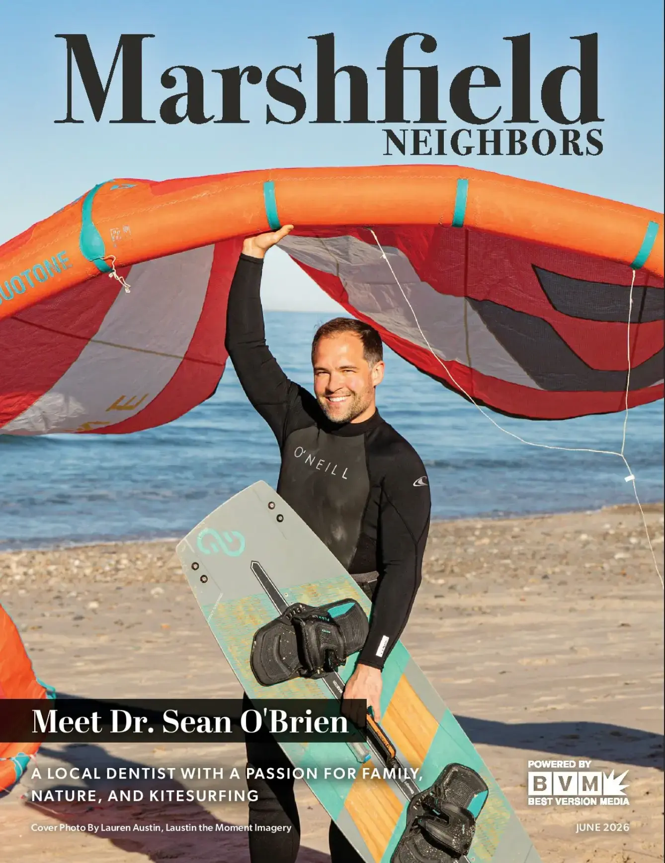 Dr. Sean O'Brien, local Duxbury dentist, holds kiteboarding equipment on beach in wetsuit.