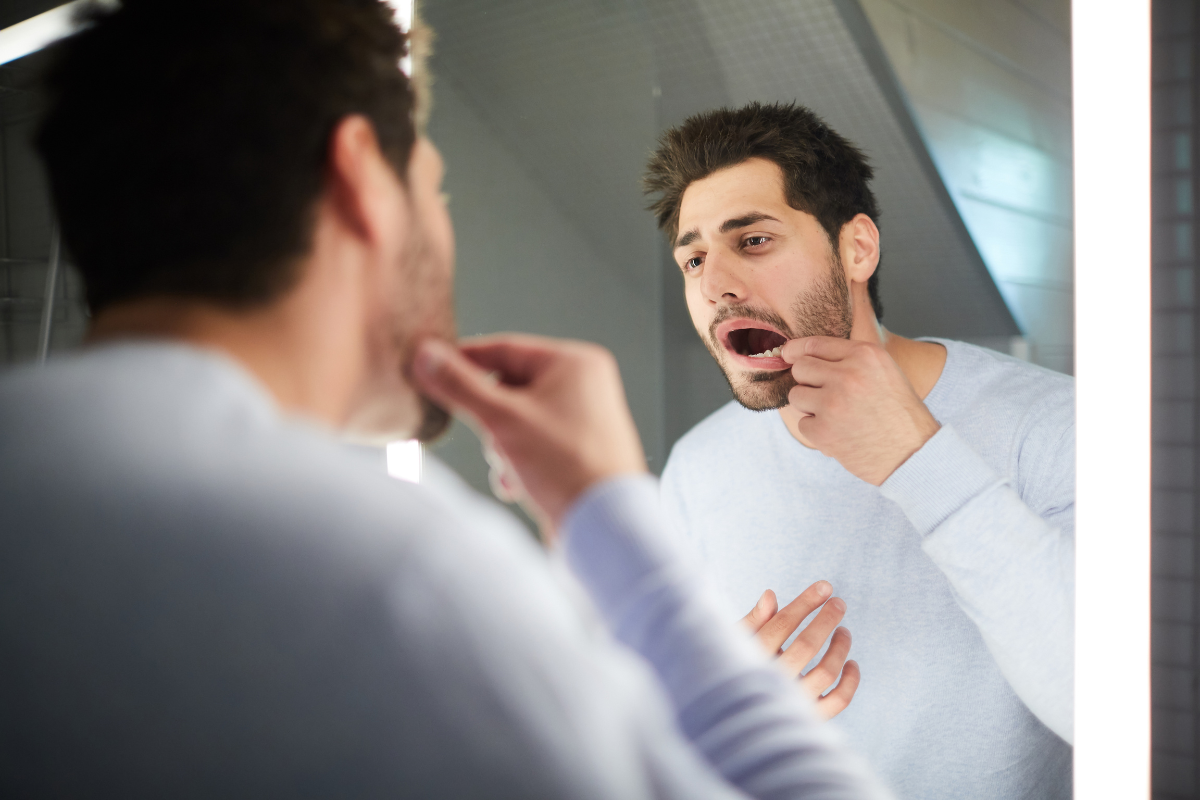 Man examining his teeth in bathroom mirror with bright lighting.