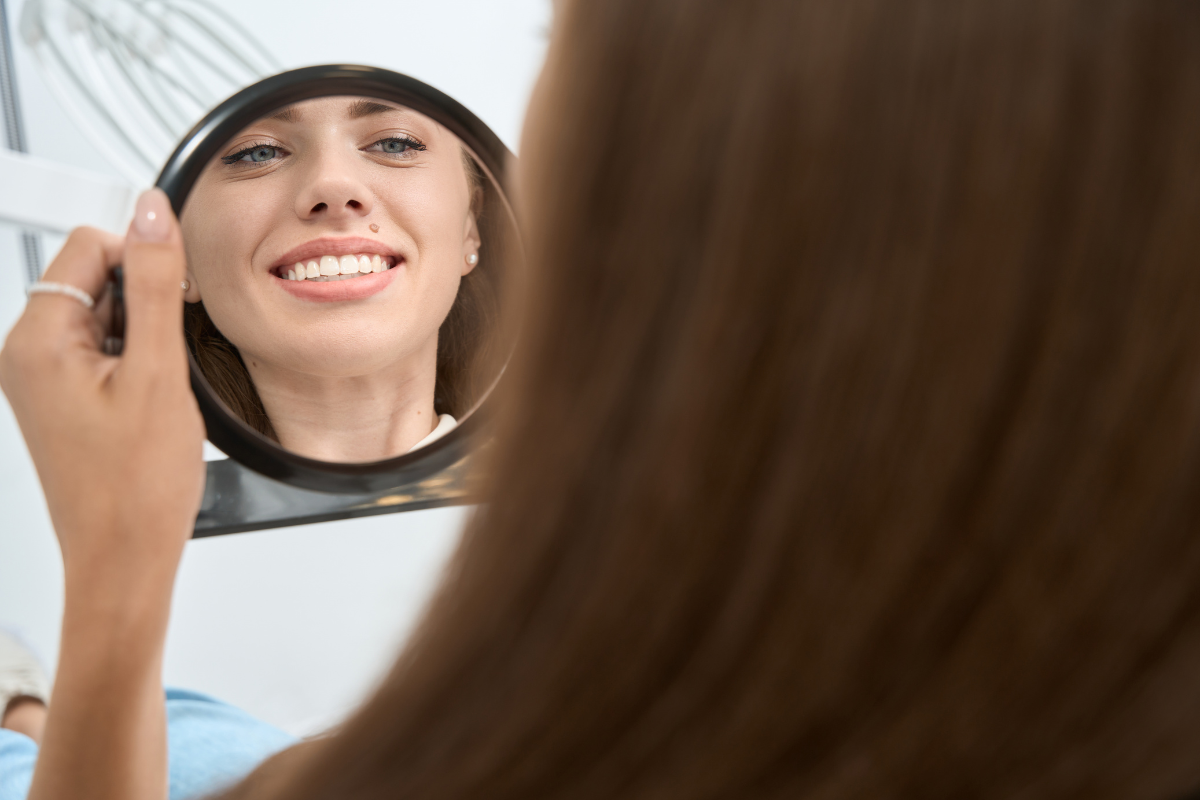 How Cosmetic Dentistry Restores Teeth Damaged by Grinding and Wear Woman smiling in mirror examining her teeth after cosmetic dental treatment in Duxbury.