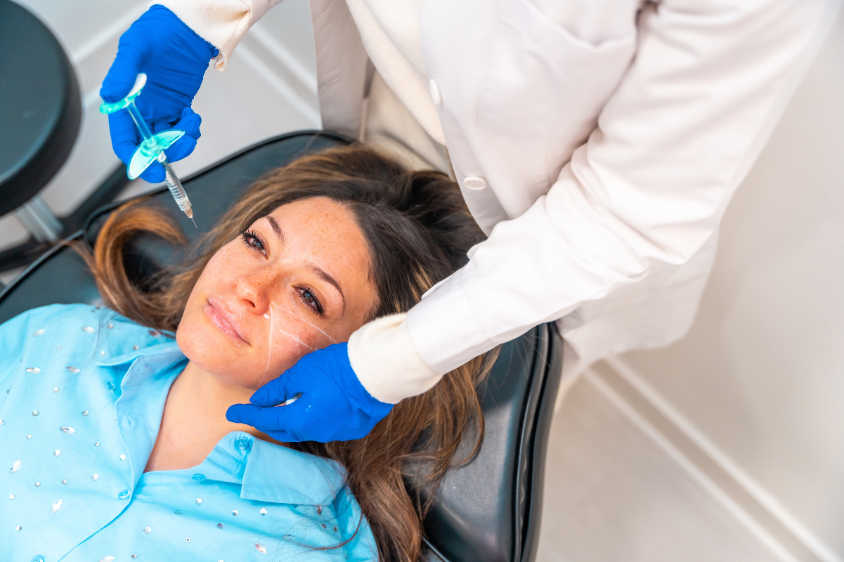 Dentist applying cosmetic treatment to patient's face during TMJ therapy session.