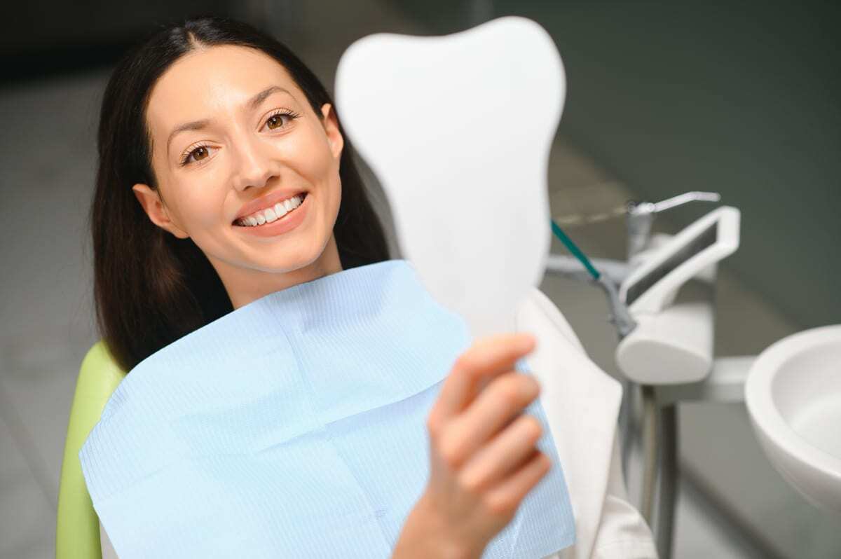 Tooth-Colored Fillings in Duxbury Smiling patient holding blue bib in dental office with chair and instruments visible.